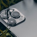 Macro shot of a smartphone with a triple camera system on leafy grass, showcasing modern technology. – apple satellite shift iphone