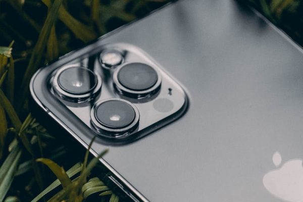 Macro shot of a smartphone with a triple camera system on leafy grass, showcasing modern technology. – apple satellite shift iphone