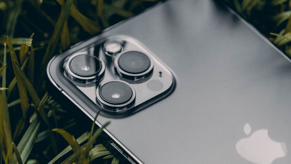 Macro shot of a smartphone with a triple camera system on leafy grass, showcasing modern technology. – apple satellite shift iphone