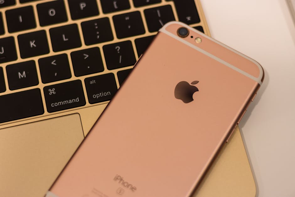 Close-up of a rose gold iPhone 6s placed on a MacBook keyboard, showcasing sleek design and modern technology.