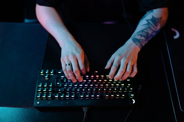 Close-up of hands typing on a RGB gaming keyboard with a tattooed arm and ring visible. – best gaming keyboards 2025