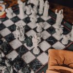 Close-up of a detailed wizard-themed chess set on a wooden table with game card. – Book of Travels price cut