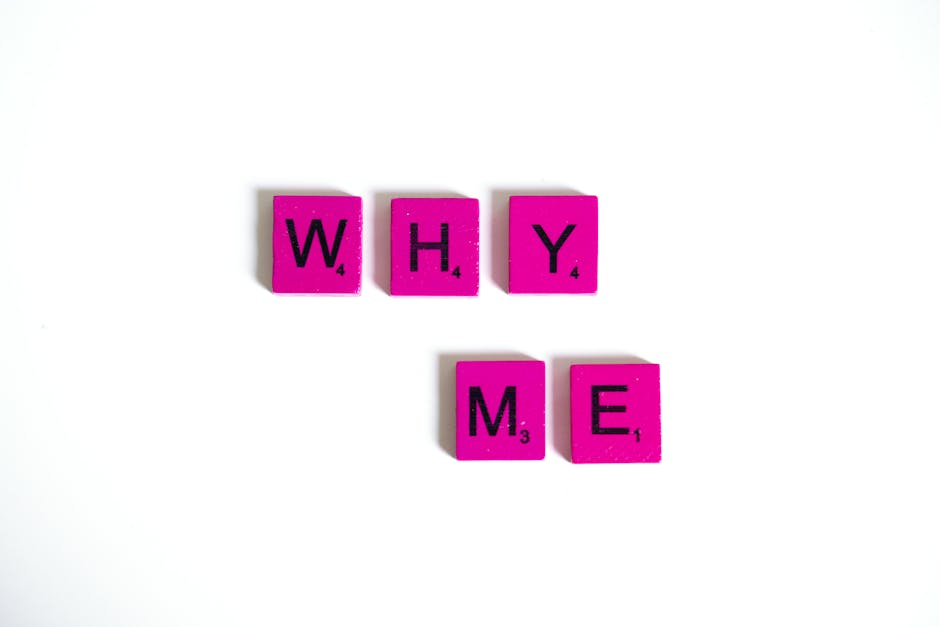 Pink Scrabble tiles form the words 'Why Me' on a white background, emphasizing questioning and introspection.