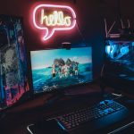 A sleek gaming setup with neon 'hello' sign, dual monitors, and illuminated PC for a futuristic vibe.