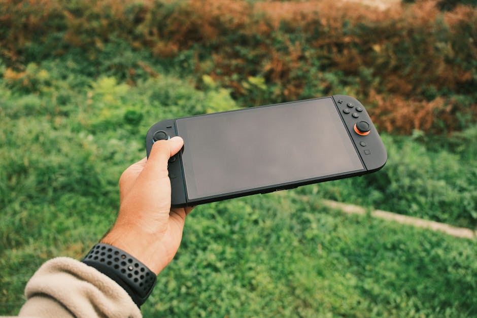 Close-up of a person's hand holding a black handheld gaming console against a green outdoor background. – China's mobile gaming dominance