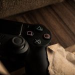 A close-up of a PlayStation gaming controller resting on a wooden surface with a rustic feel. – Fragmentary Order Official Announcement