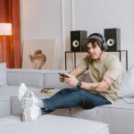 Young man sitting on a couch, enjoying video gaming at home with headphones on. – home game room setup