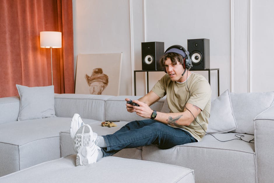 Young man sitting on a couch, enjoying video gaming at home with headphones on. – home game room setup
