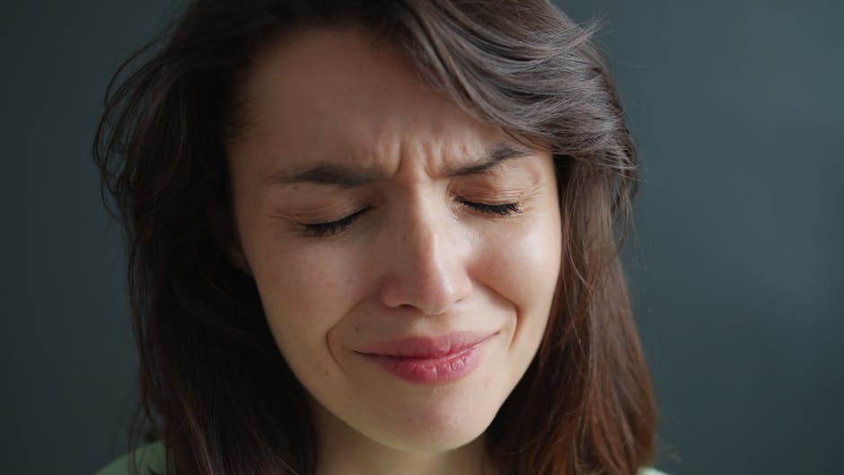 Close-up of a woman expressing emotion with eyes closed and a frown.