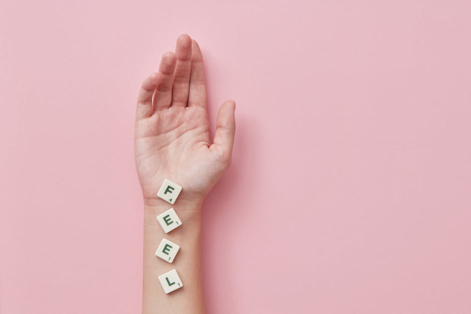 A minimalist photograph of a hand laid on pink background spelling 'FEEL' with Scrabble tiles.