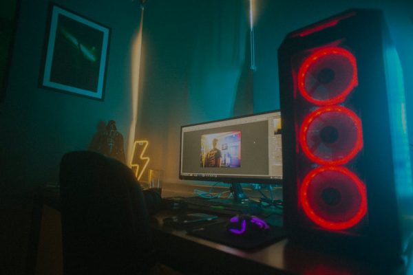 Atmospheric photo of a gaming setup with a glowing PC case and monitor displaying content editing software.