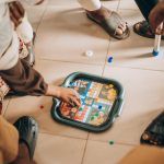 Group of children playing board game indoors on a tiled floor, focused on the game pieces. – Ludum Dare 59 impact