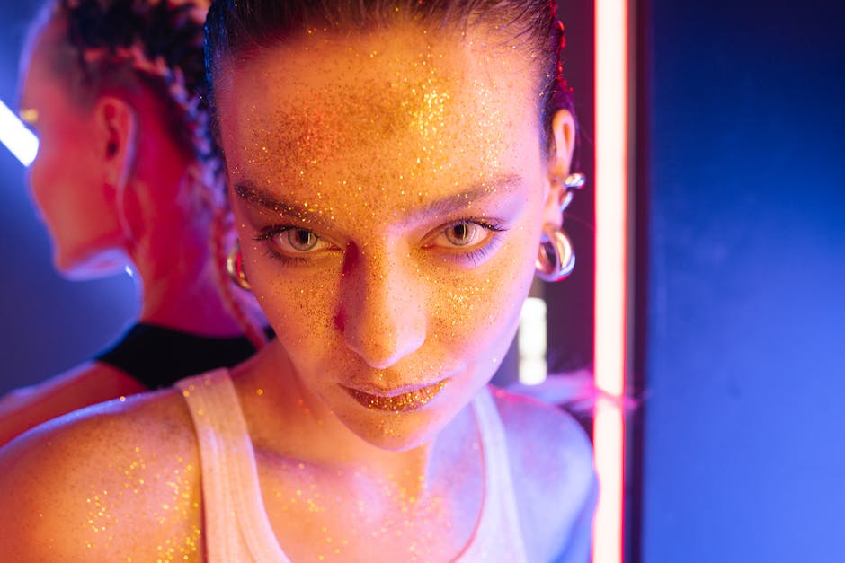 Close-up portrait of a woman with glitter makeup, standing under vibrant neon lights with earrings visible.