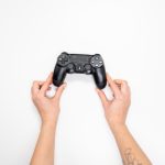 Top view of hands holding a black gaming controller against a white background. – left-handed controls in modern games