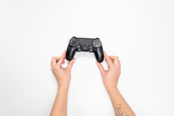 Top view of hands holding a black gaming controller against a white background. – left-handed controls in modern games