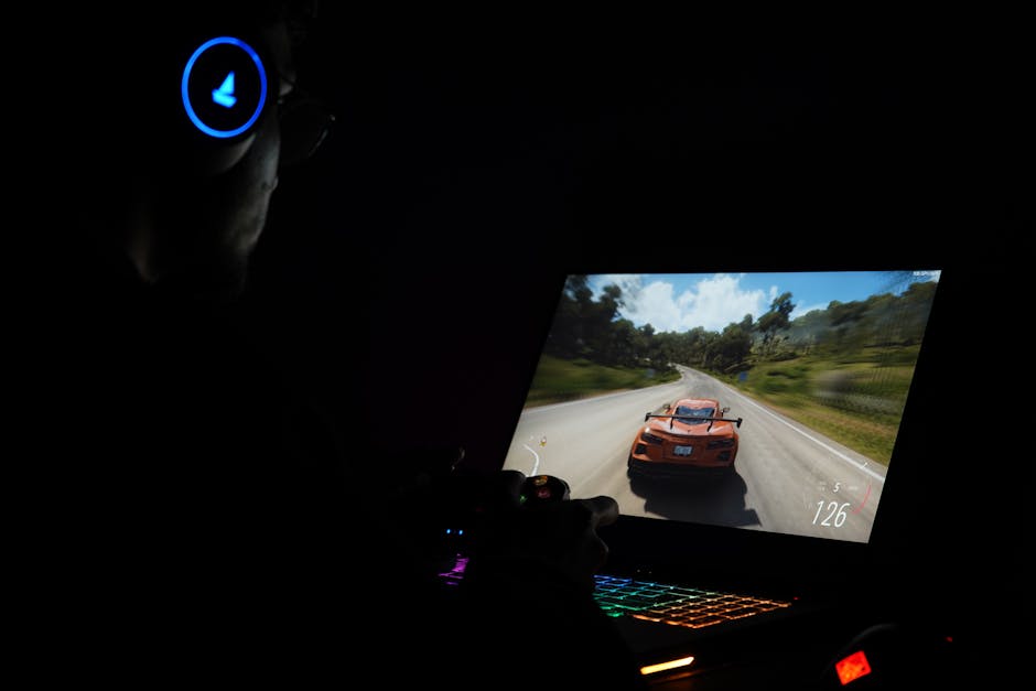 A gamer using a laptop and headphones to play a car racing game in a dark setting. – Replaced Steam Release