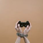 Conceptual image of hands in chains holding a game controller symbolizing gaming addiction. – parental controls for social