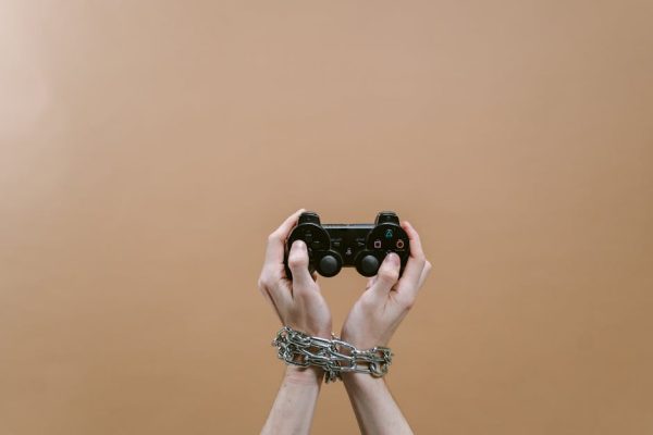 Conceptual image of hands in chains holding a game controller symbolizing gaming addiction. – parental controls for social