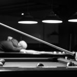 Black and white image of people playing billiards indoors, focusing on cue stick action. – Spooky Snooker Game Review