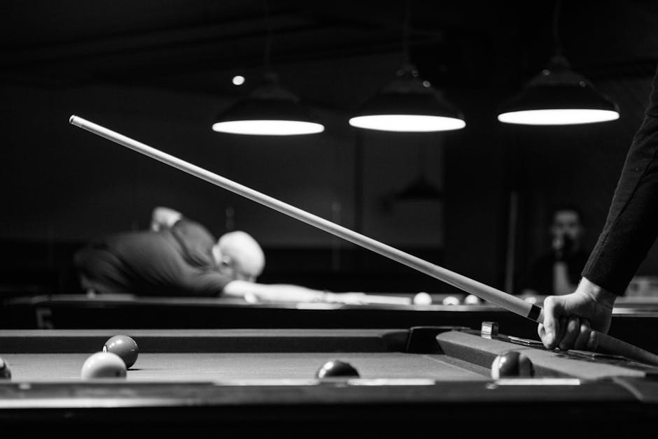 Black and white image of people playing billiards indoors, focusing on cue stick action. – Spooky Snooker Game Review