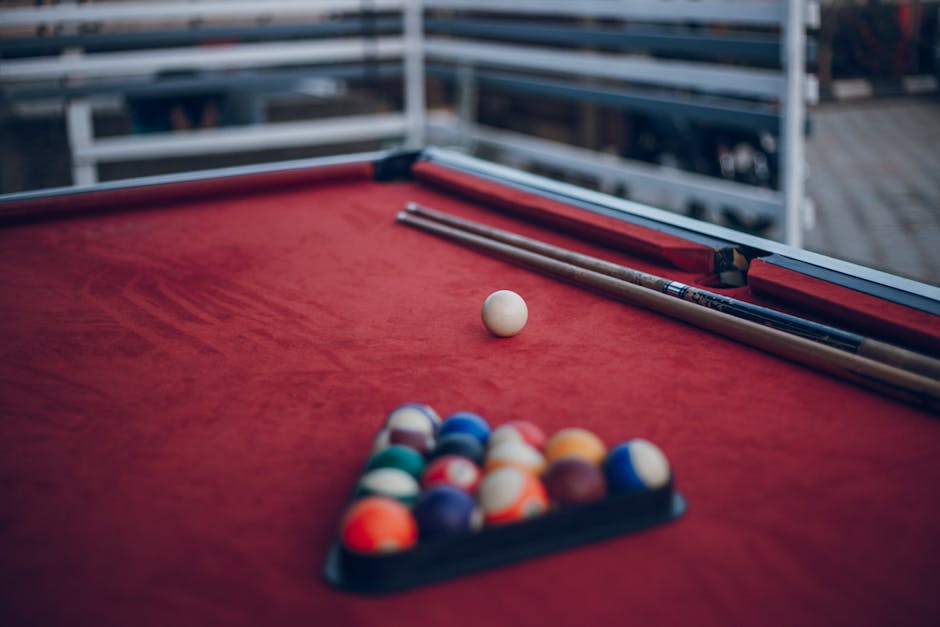 Red pool table setup with cue sticks and arranged billiard balls, ready for a game.