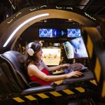 A woman plays a video game in a high-tech scorpion gaming chair, immersed in a modern arcade. – Subnautica 2 publisher change