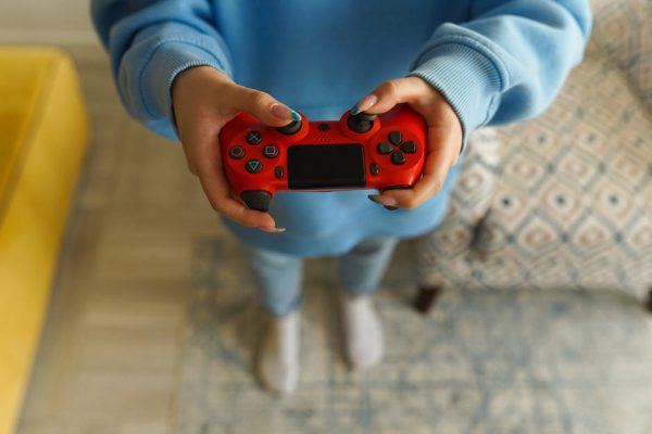Person holding a bright red gaming controller indoors, focusing on gameplay. – mass layoffs in video games