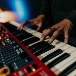 Close-up of hands playing a synthesizer keyboard in a moody, dimly lit environment. – best keyboards 2026