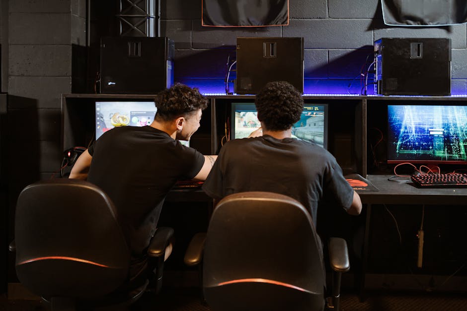 Two young men engaged in intense gaming session at an eSports venue. Computers and ambient lighting create an <a href=